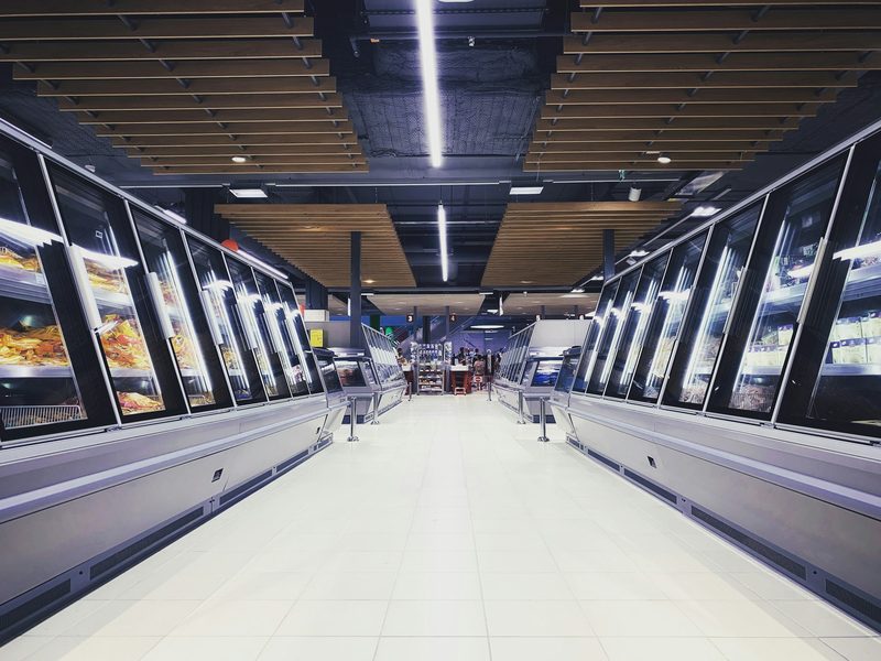 A bright grocery aisle leading to refrigerated cases